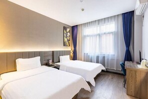 Quarto de hotel com duas camas, uma escrivaninha e uma janela com cortinas.