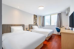 Quarto de hotel com duas camas, uma escrivaninha, uma cadeira, uma janela com cortinas e um aparelho de ar condicionado.