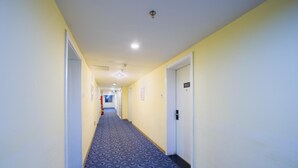 Un couloir d’hôtel avec un tapis à motifs bleus, des murs jaunes et une porte portant le numéro 512.