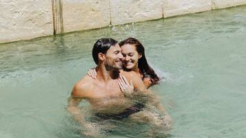 A man and a woman in a shallow pool with a stone wall in the background.