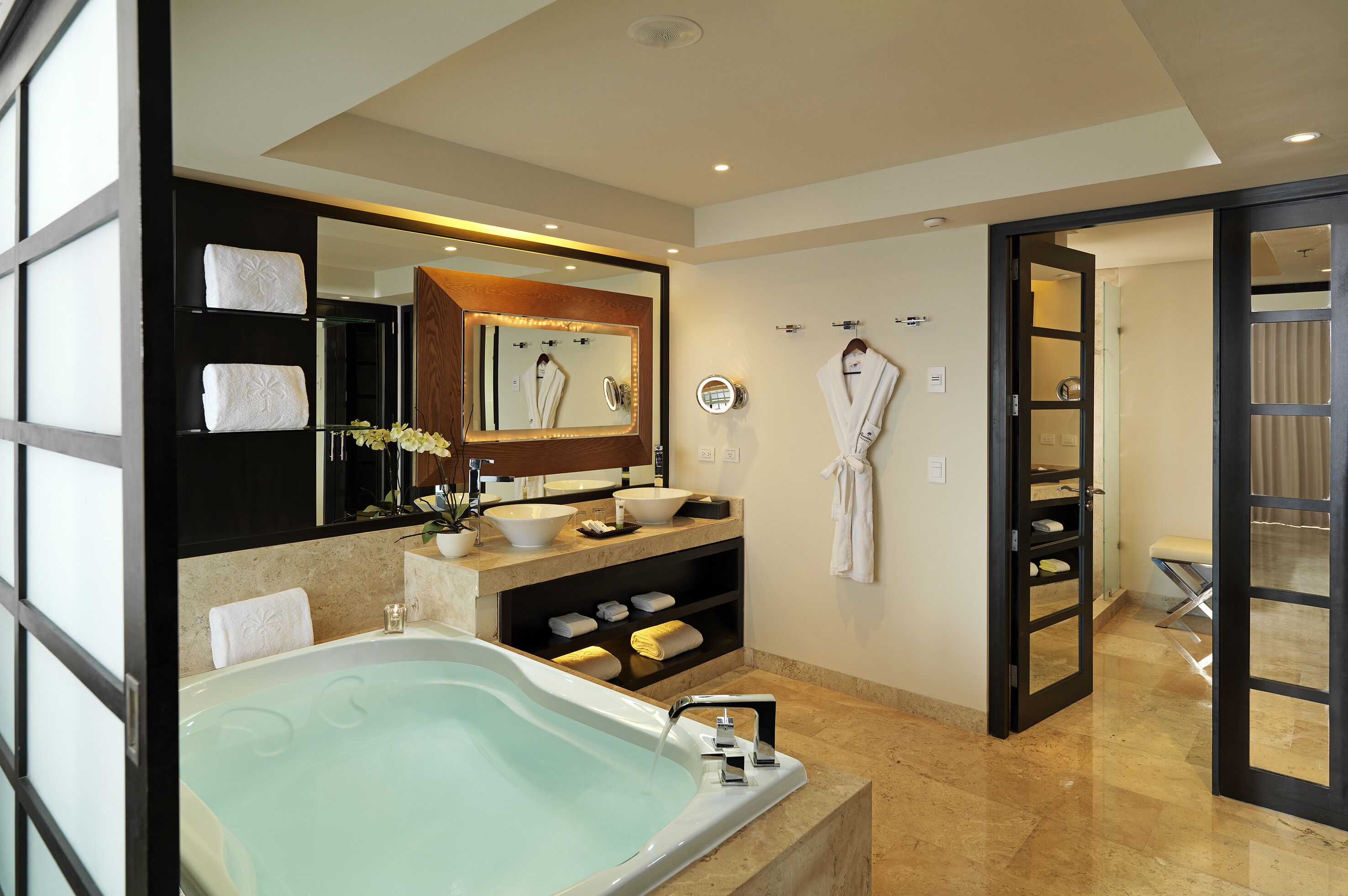 A modern bathroom with a large bathtub, a vanity with a mirror, and a robe hanging on the wall.