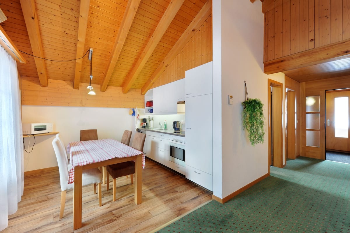 Una cocina compacta con vigas de madera, una mesa de comedor con sillas y un refrigerador pequeño.