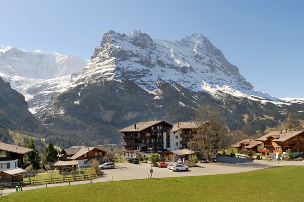 A mountain resort with chalet-style buildings, a parking area, and a view of snow-capped peaks.