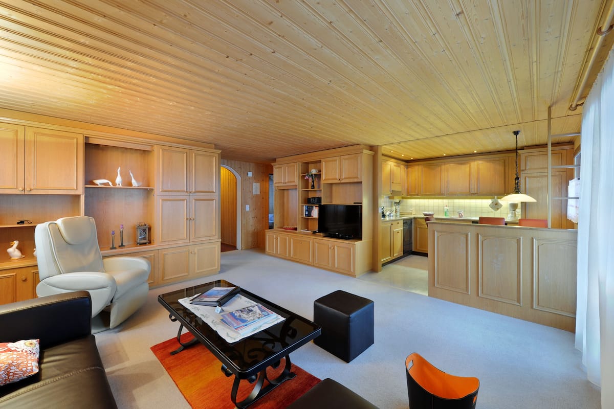 Amplia sala de estar con sofá, mesa de centro y zona de cocina con armarios de madera y televisor.