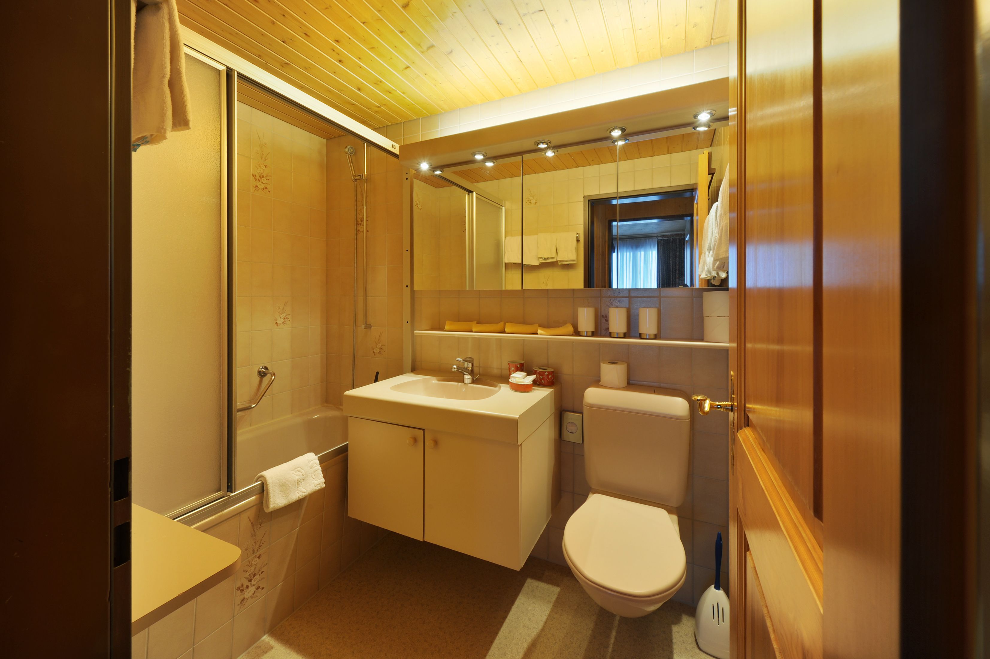 A modern bathroom with a wooden ceiling, a sink, a toilet, and a mirror.