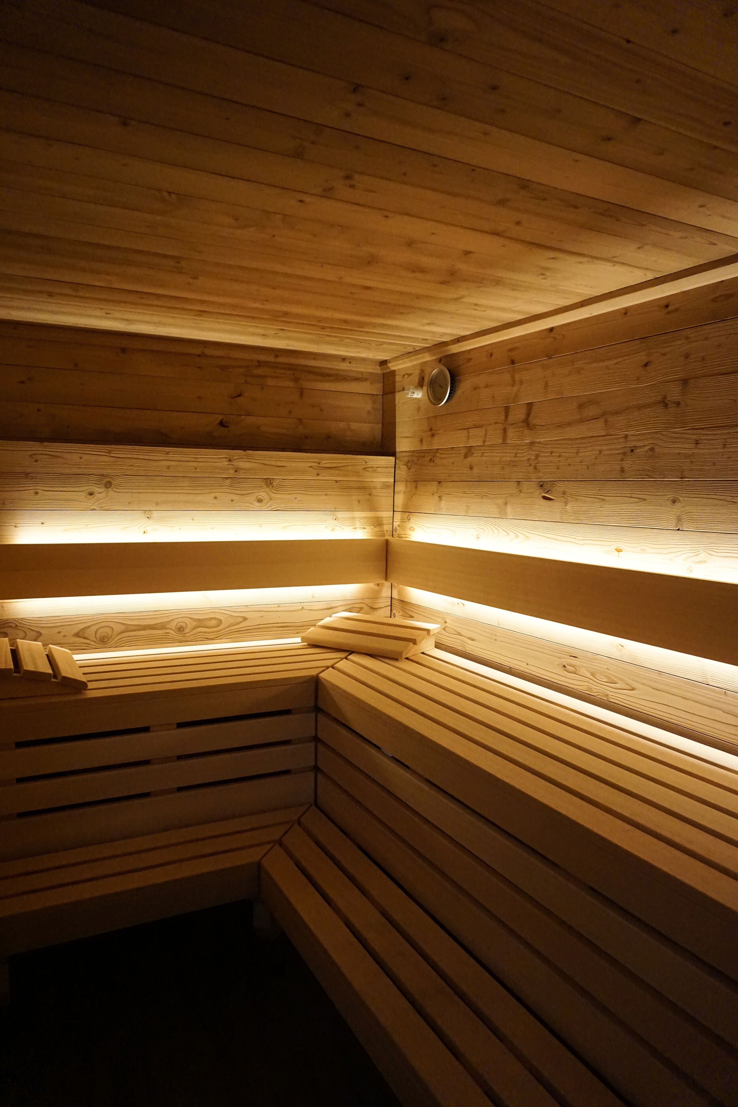 A sauna with wooden benches and slatted walls, illuminated by overhead lights.