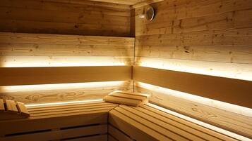 A sauna with wooden benches and slatted walls, illuminated by overhead lights.