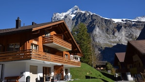 Een houten chalet met balkon, met op de achtergrond een berg met sneeuw.