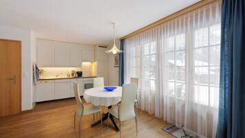 Una cocina moderna con armarios blancos, una mesa de comedor con sillas y un amplio ventanal con cortinas ligeras.