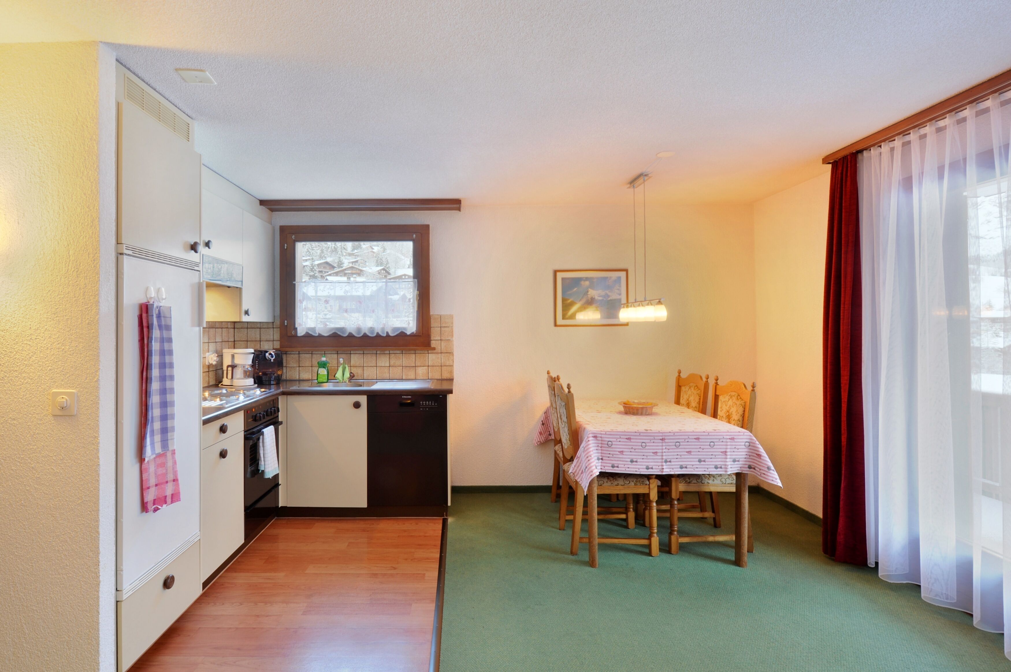 Cocina compacta con comedor, que incluye una mesa con sillas, una ventana con cortinas y una lámpara colgante.