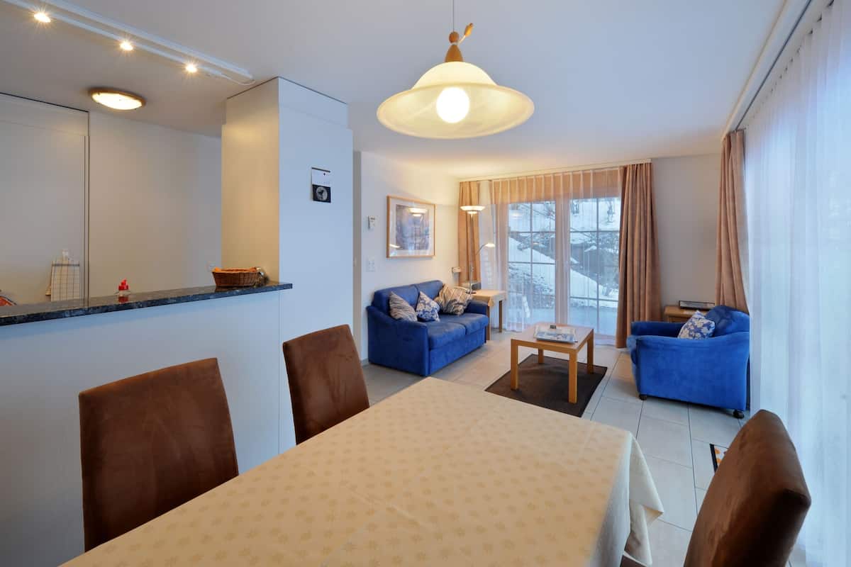 Una sala de estar moderna con una mesa de comedor, dos sofás azules y un amplio ventanal con cortinas.