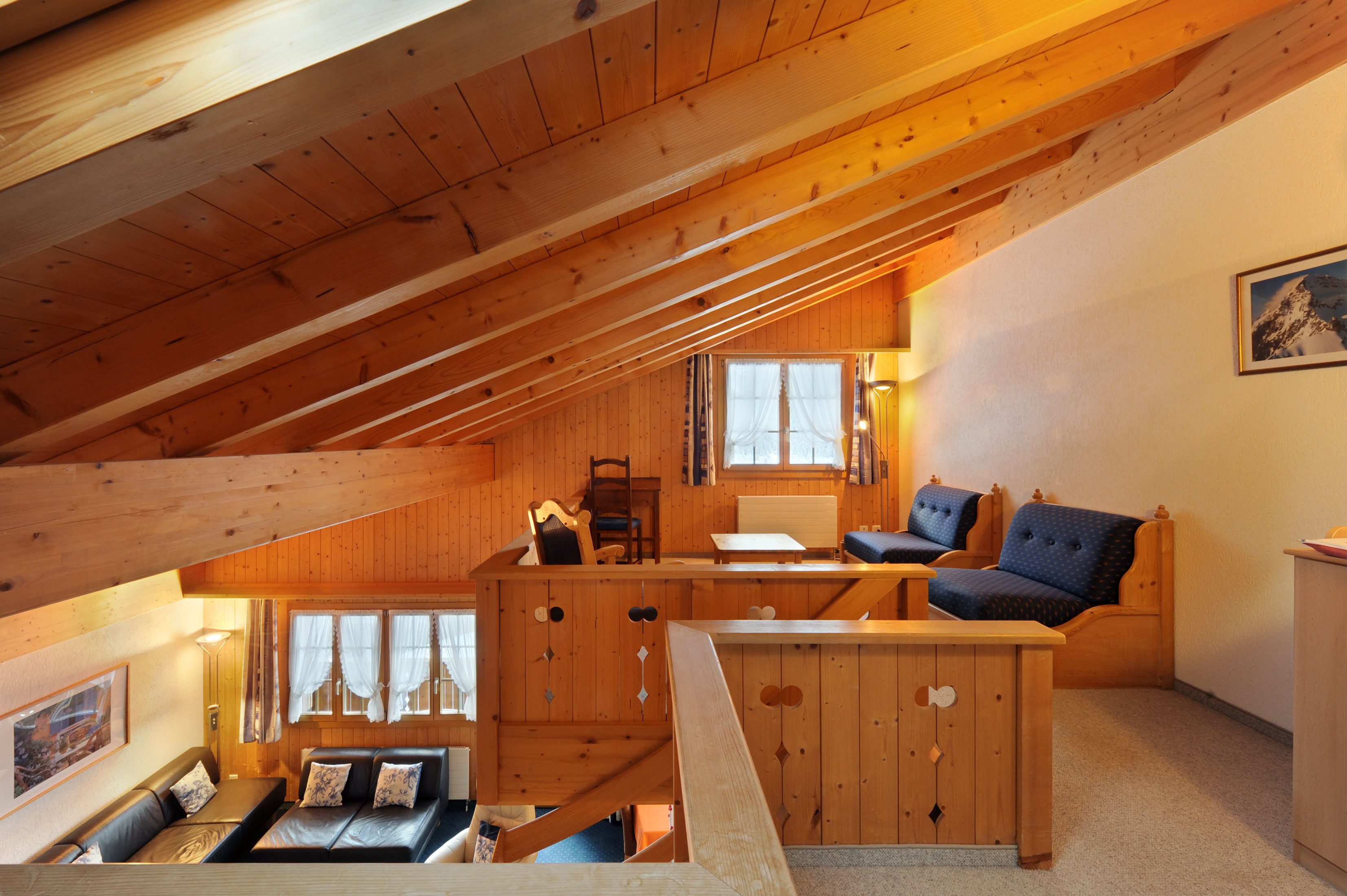 Interior acogedor de una cabaña con dormitorio en altillo, paredes de madera, comedor y sala de estar con sofá y sillones.