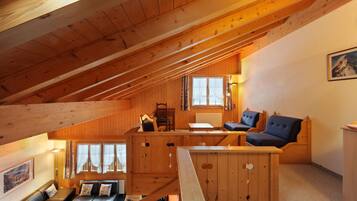 Interior acogedor de una cabaña con dormitorio en altillo, paredes de madera, comedor y sala de estar con sofá y sillones.