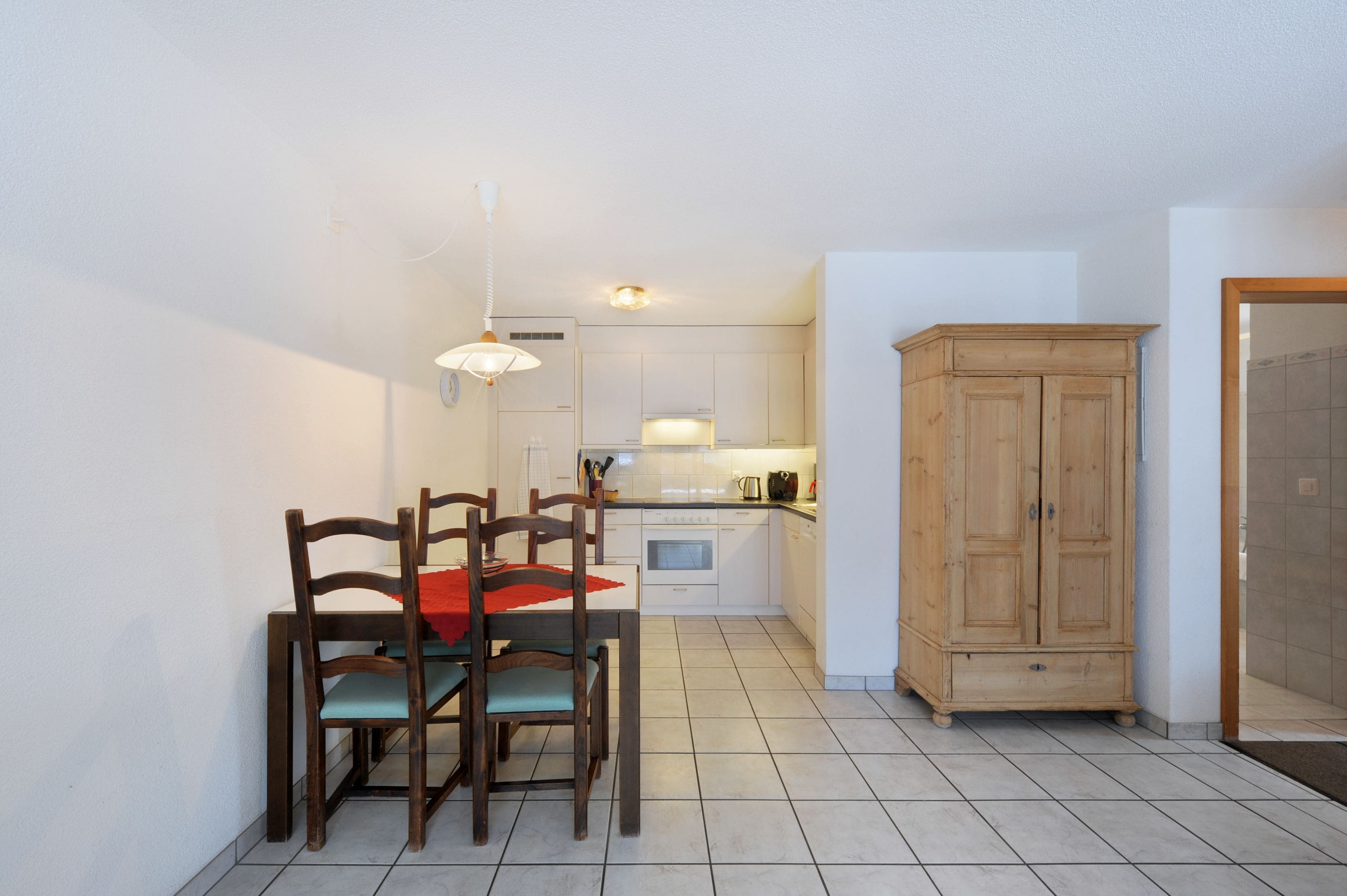 Une cuisine compacte avec des meubles blancs, un meuble en bois et un coin repas comprenant deux chaises et une table.