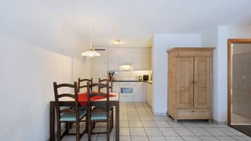 Une cuisine compacte avec des meubles blancs, un meuble en bois et un coin repas comprenant deux chaises et une table.