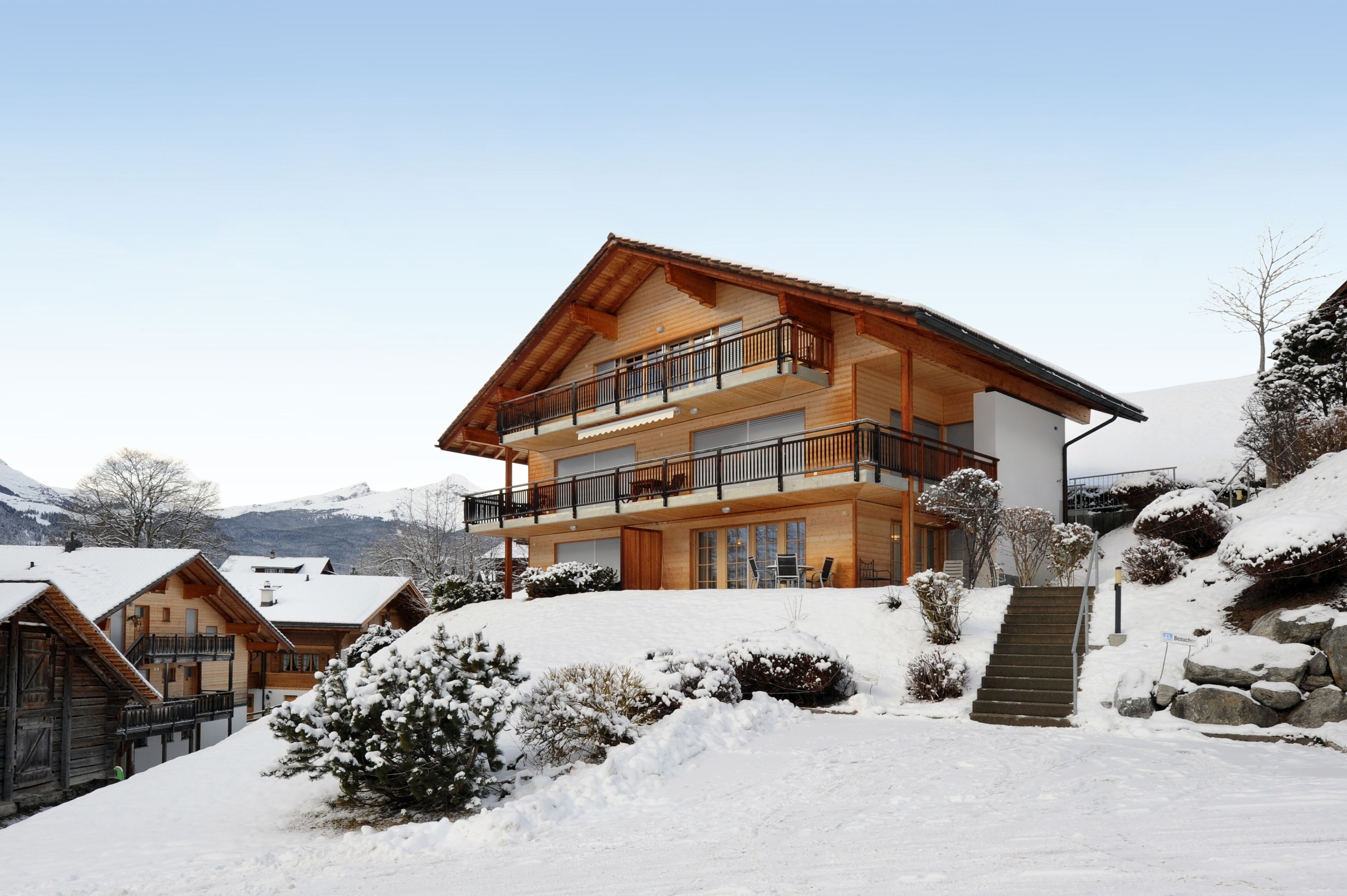 Un chalet in legno a due piani con balconi, immerso in un paesaggio montano innevato.