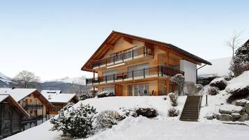 Un chalet in legno a due piani con balconi, immerso in un paesaggio montano innevato.