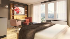 Een hotelkamer met een bed, een bureau, een stoel, een televisie en een raam met uitzicht op de bergen.