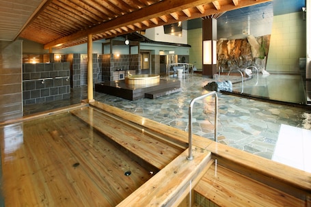 A wooden spa area with a hot tub, stone flooring, and a glass wall reflecting the interior.