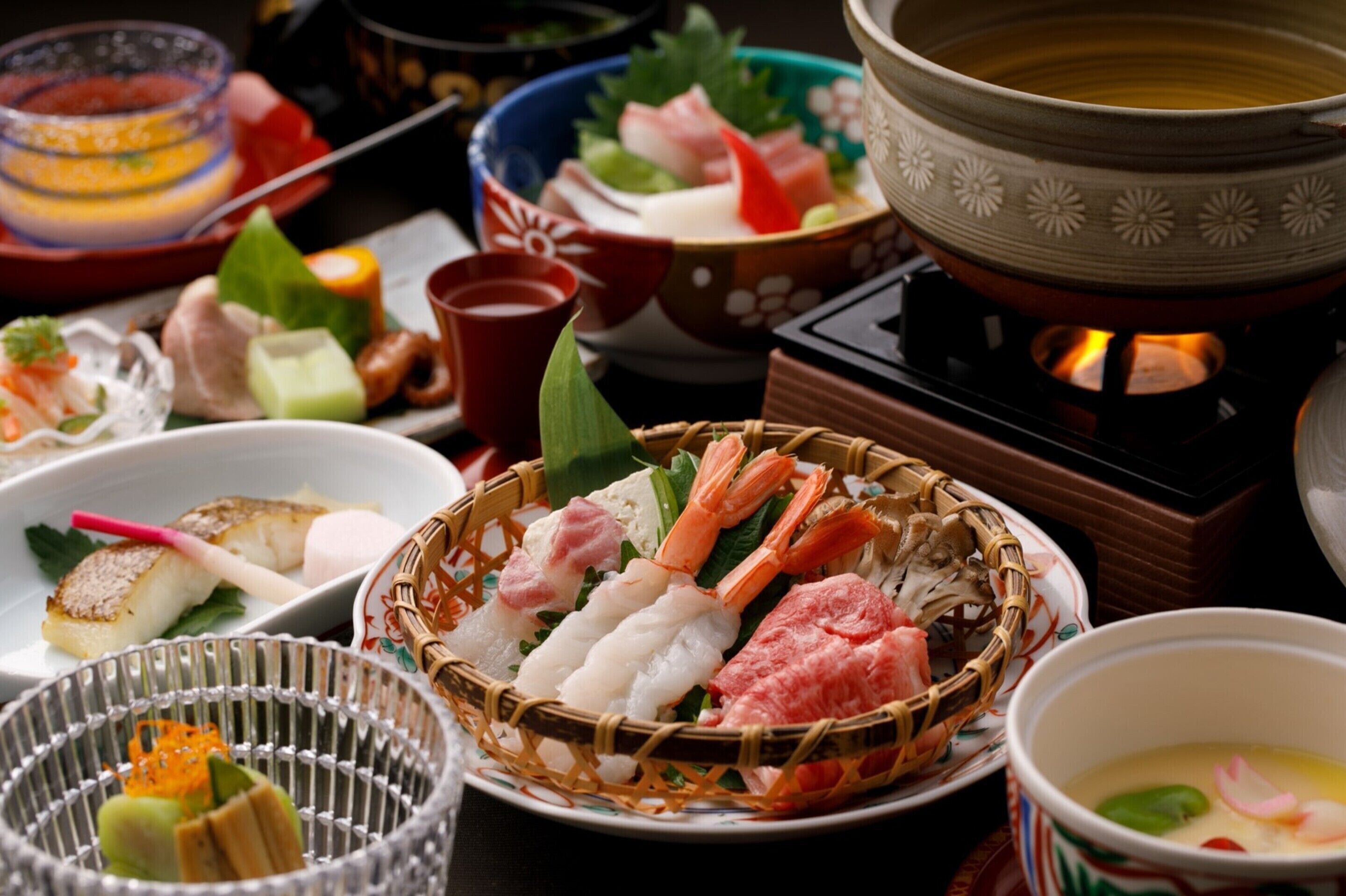 A variety of Japanese dishes, including sushi and sashimi, arranged on a table with a traditional tea set and a hot pot.