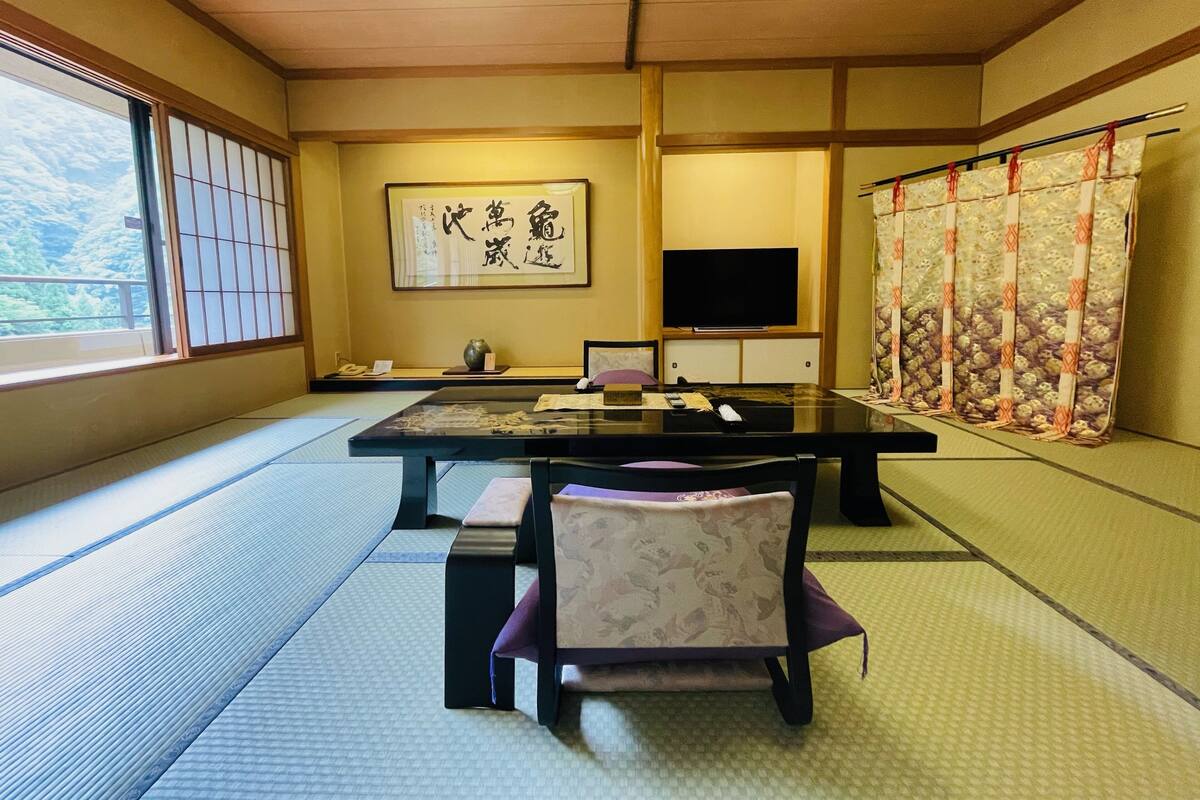 A traditional Japanese room with tatami flooring, a low table, a television, and a shoji screen.