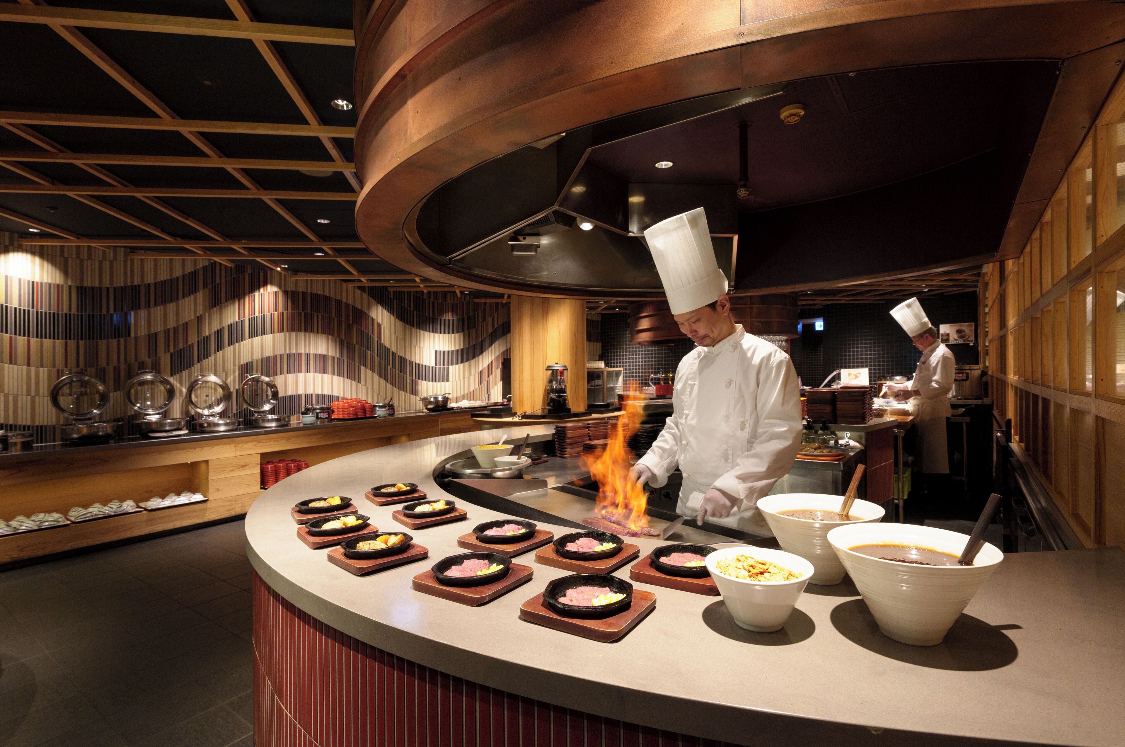 A chef cooking at a counter with a modern kitchen design, including a curved ceiling and wooden accents.