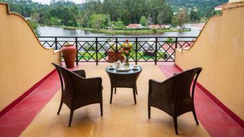 A balcony with wicker chairs and a table, overlooking a lake and greenery.