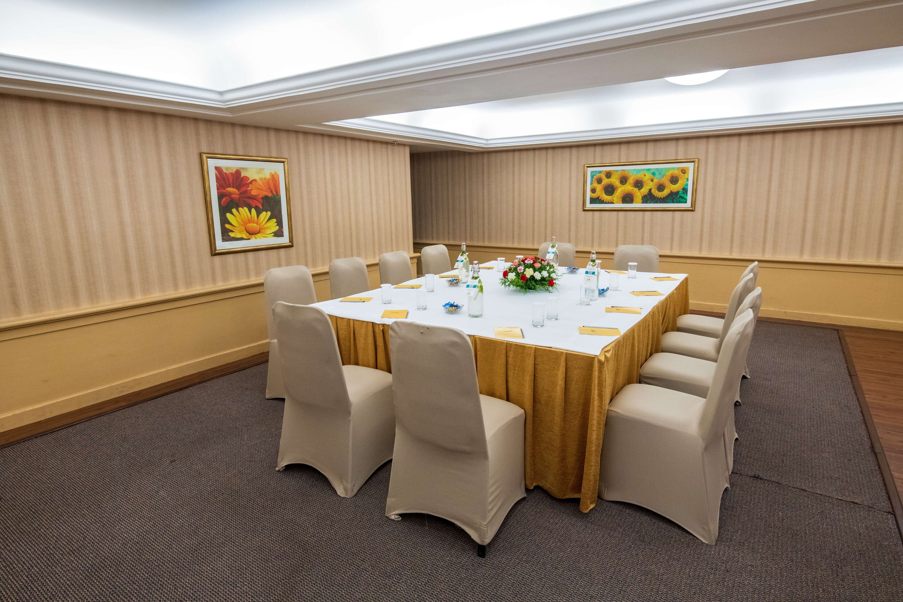 A conference room with a large table, beige chairs, and floral decorations.