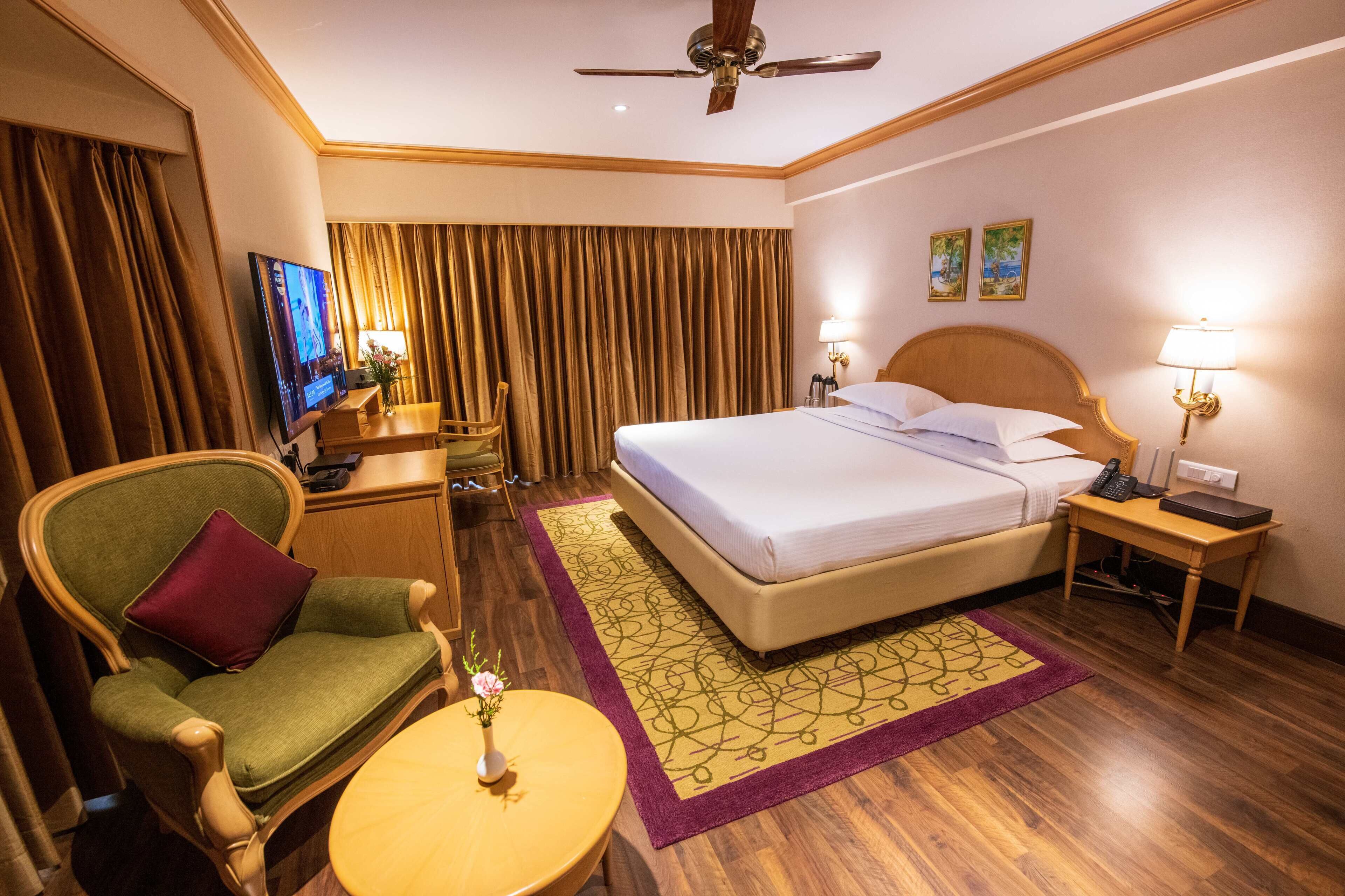 A hotel room with a bed, a chair, a desk, a television, and a ceiling fan.