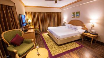 A hotel room with a bed, a chair, a desk, a television, and a ceiling fan.