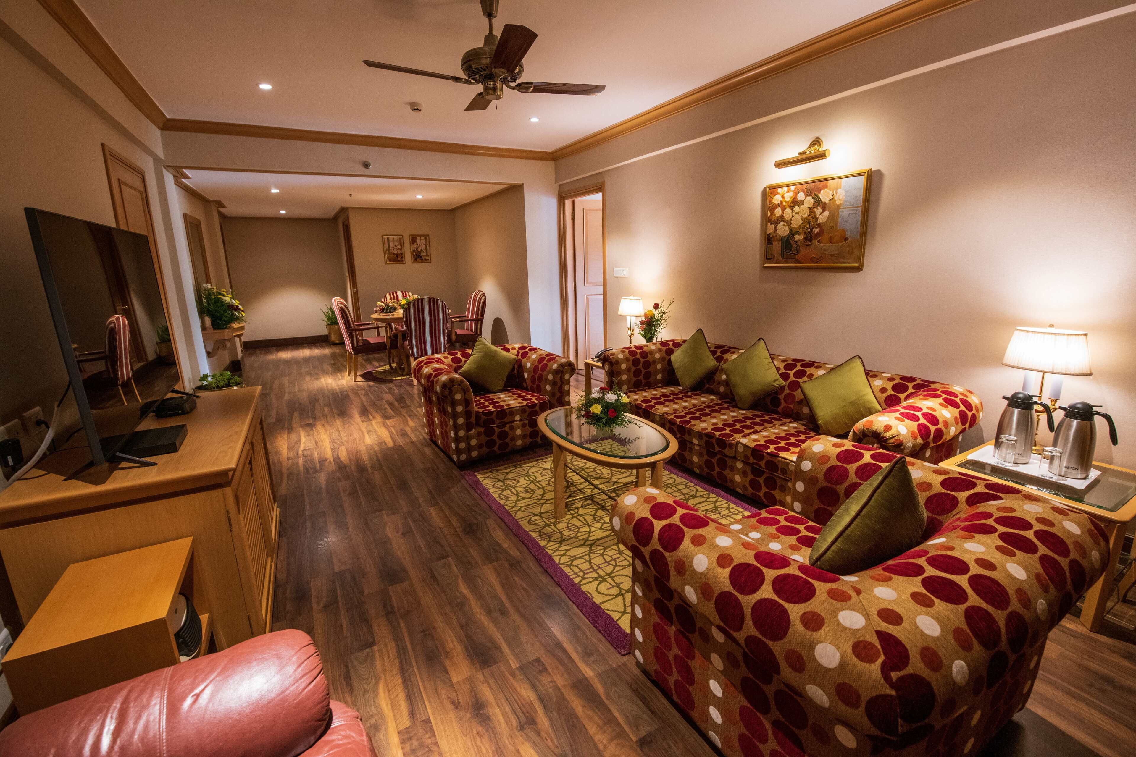 A hotel living room with a sofa set, a coffee table, a TV, and a desk.