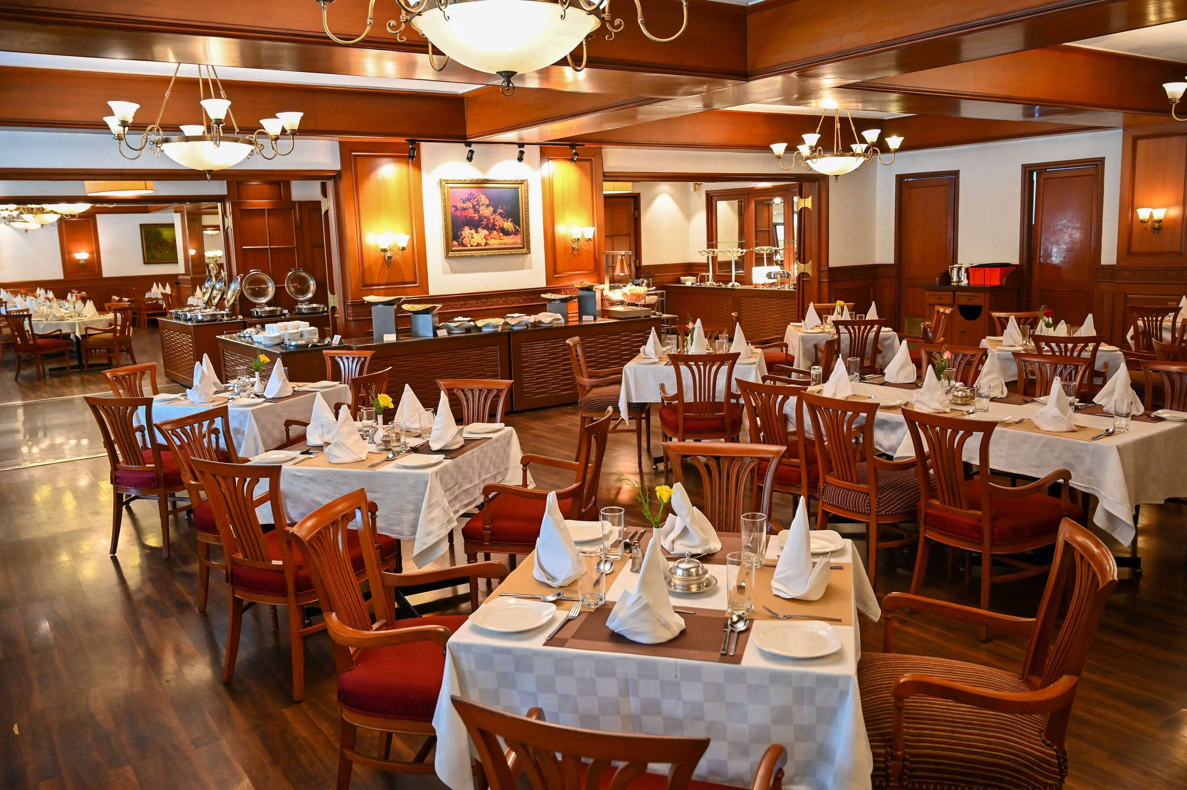 A spacious dining area with multiple tables set for service, wooden chairs, and a central buffet station.