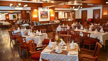 A spacious dining area with multiple tables set for service, wooden chairs, and a central buffet station.