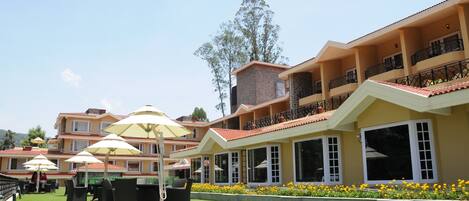 A hotel with multiple balconies, outdoor seating with umbrellas, and a well-maintained lawn.