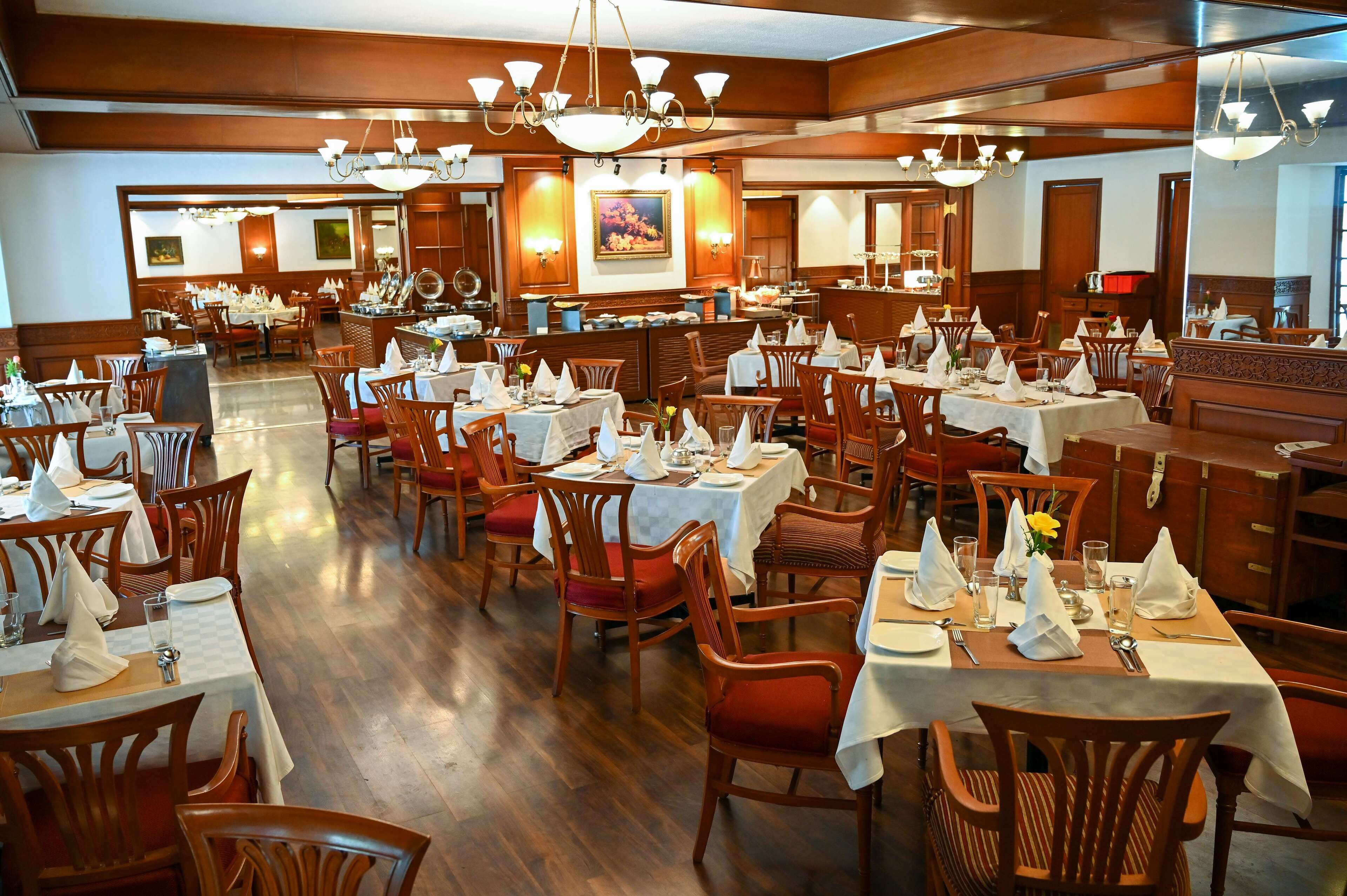 Un restaurante espacioso con varias mesas y sillas, suelo de madera y candelabros.