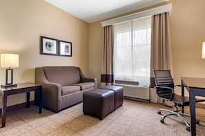 A hotel room with a sofa, a desk, a chair, and a large window with curtains. - Comfort Inn & Suites Scott-West Lafayette (Scott)