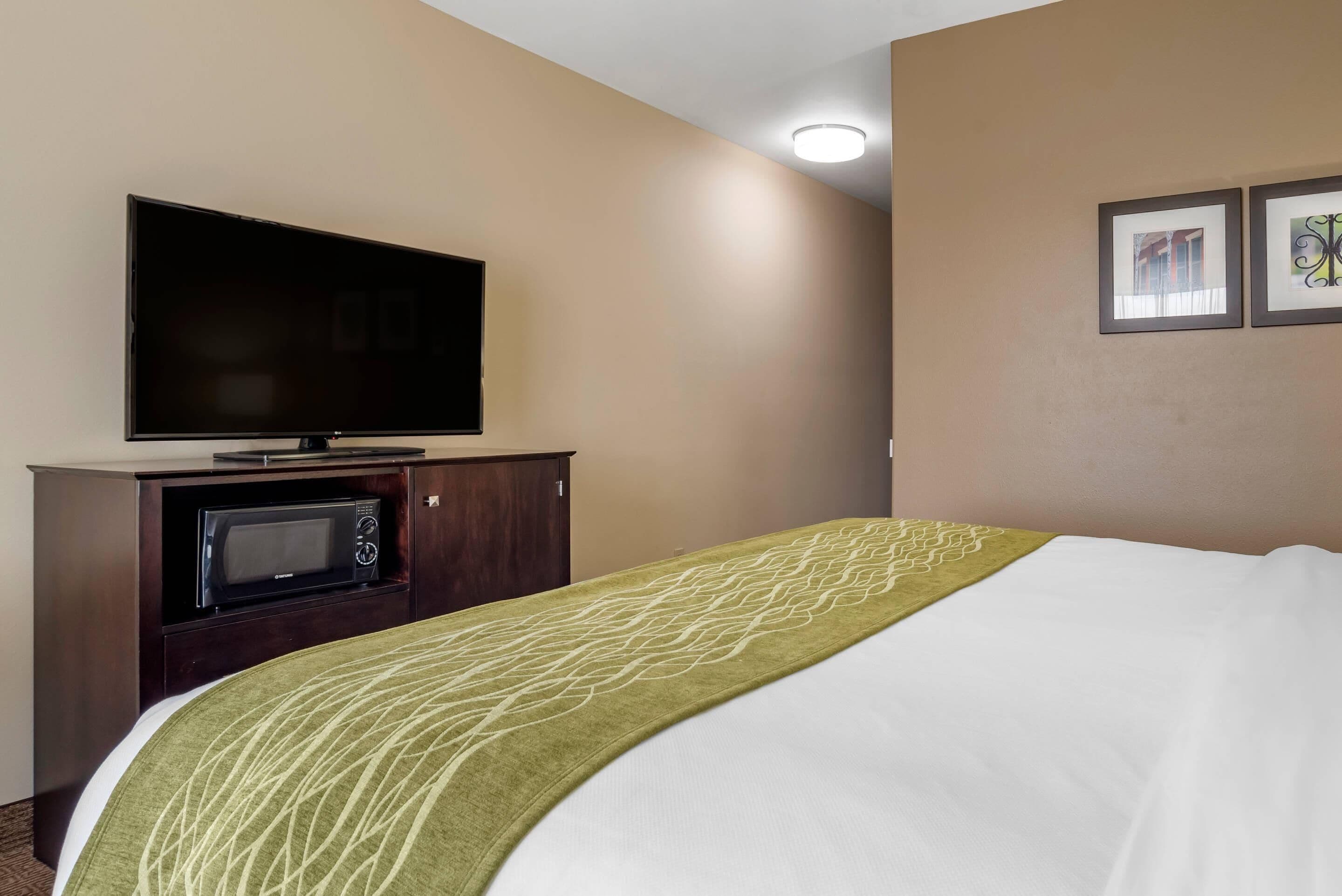 Una habitación de hotel con una cama, un televisor de pantalla plana, un microondas y un armario.