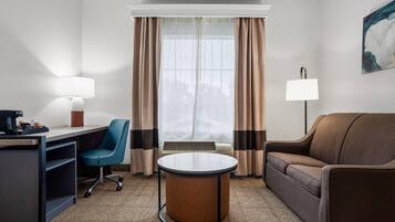 A hotel room with a desk, chair, sofa, and a round table.