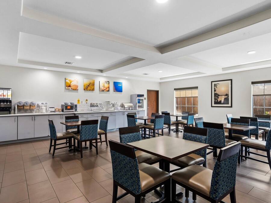 A hotel dining area with multiple tables and chairs, a kitchen area with appliances, and artwork on the walls.