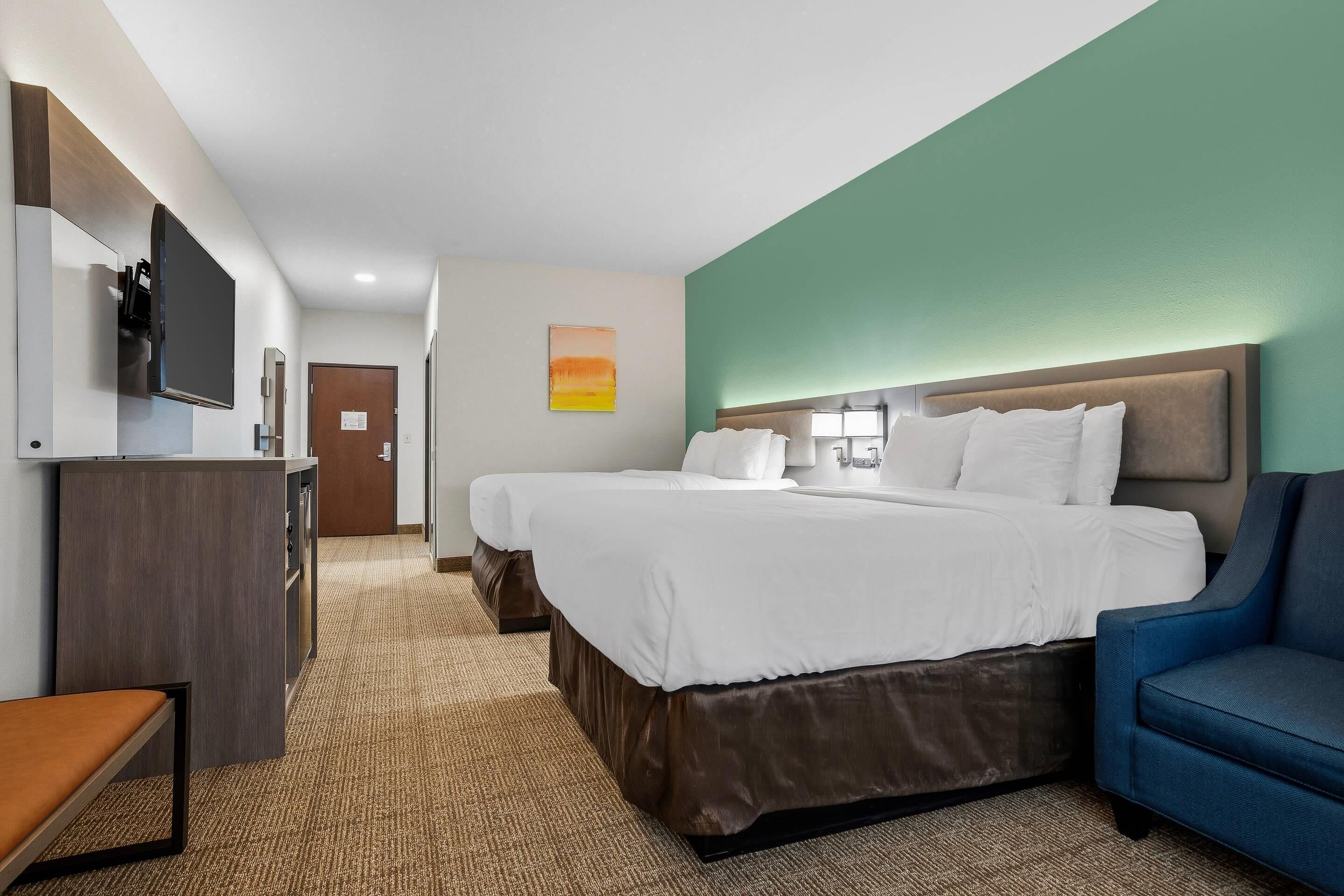 Quarto de hotel com duas camas, uma mesa, uma cadeira, uma televisão e um quadro na parede.