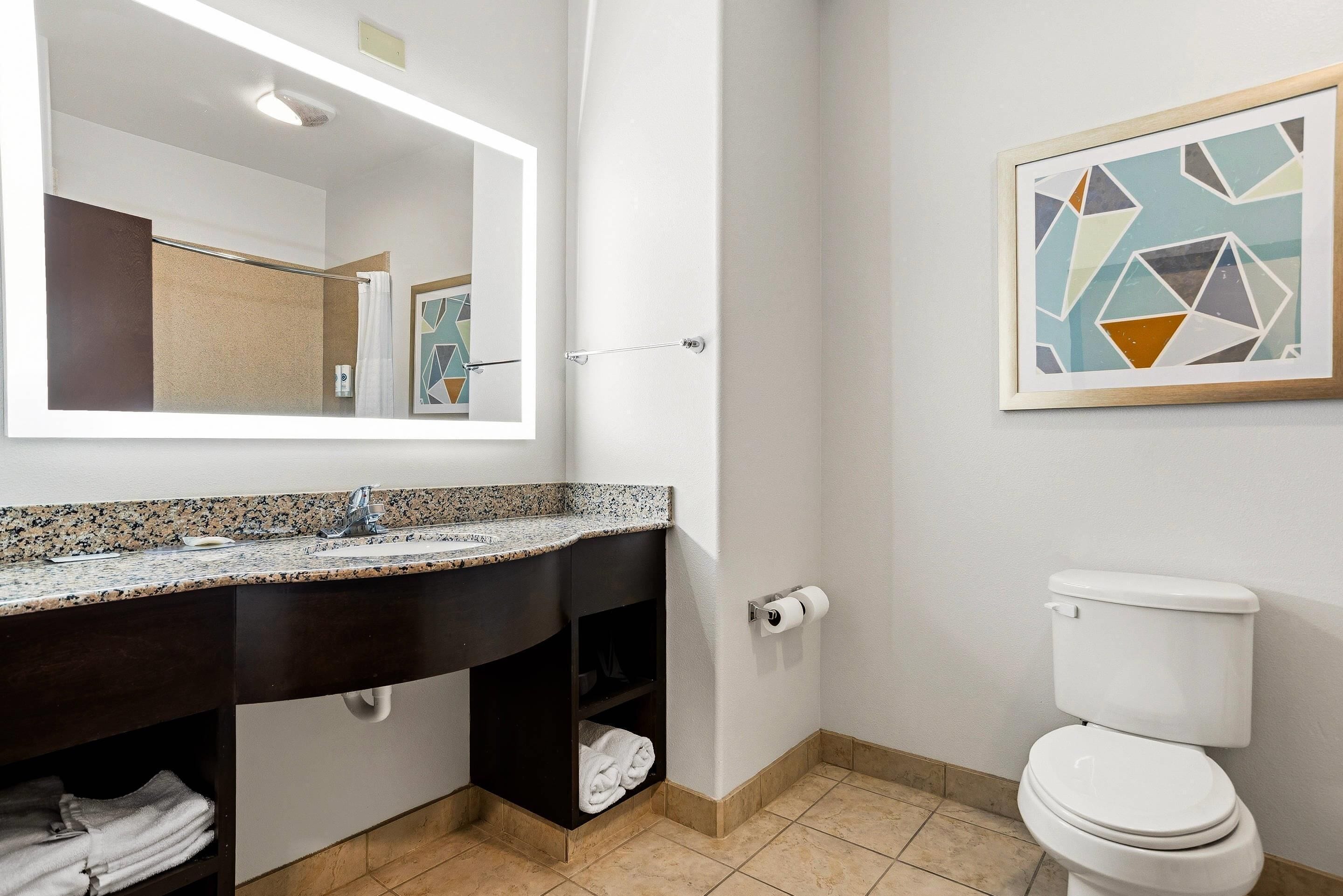 Un baño con lavamanos de granito, un espejo, inodoro y un perchero para toallas.