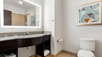 Un baño con lavamanos de granito, un espejo, inodoro y un perchero para toallas.