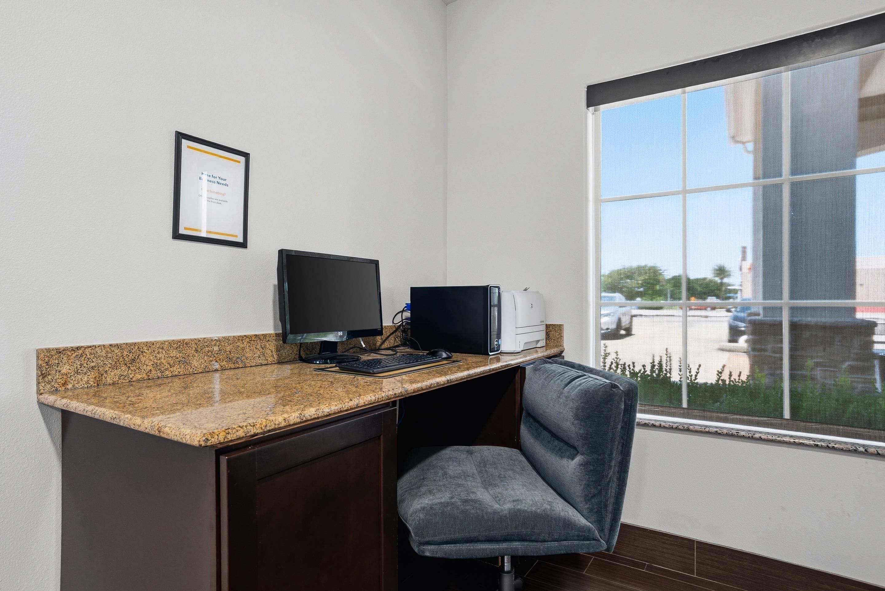 Un espace de travail comprenant un ordinateur de bureau, un écran, une imprimante et une chaise.