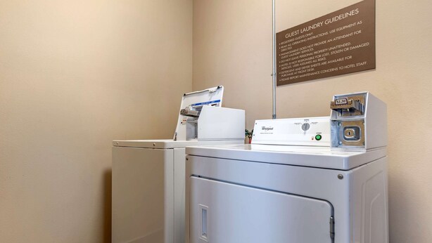 A hotel laundry area with Whirlpool washers and dryers, a sign with guest laundry guidelines, and a Whirlpool self-service machine. - Comfort Inn & Suites Scott-West Lafayette (Scott)