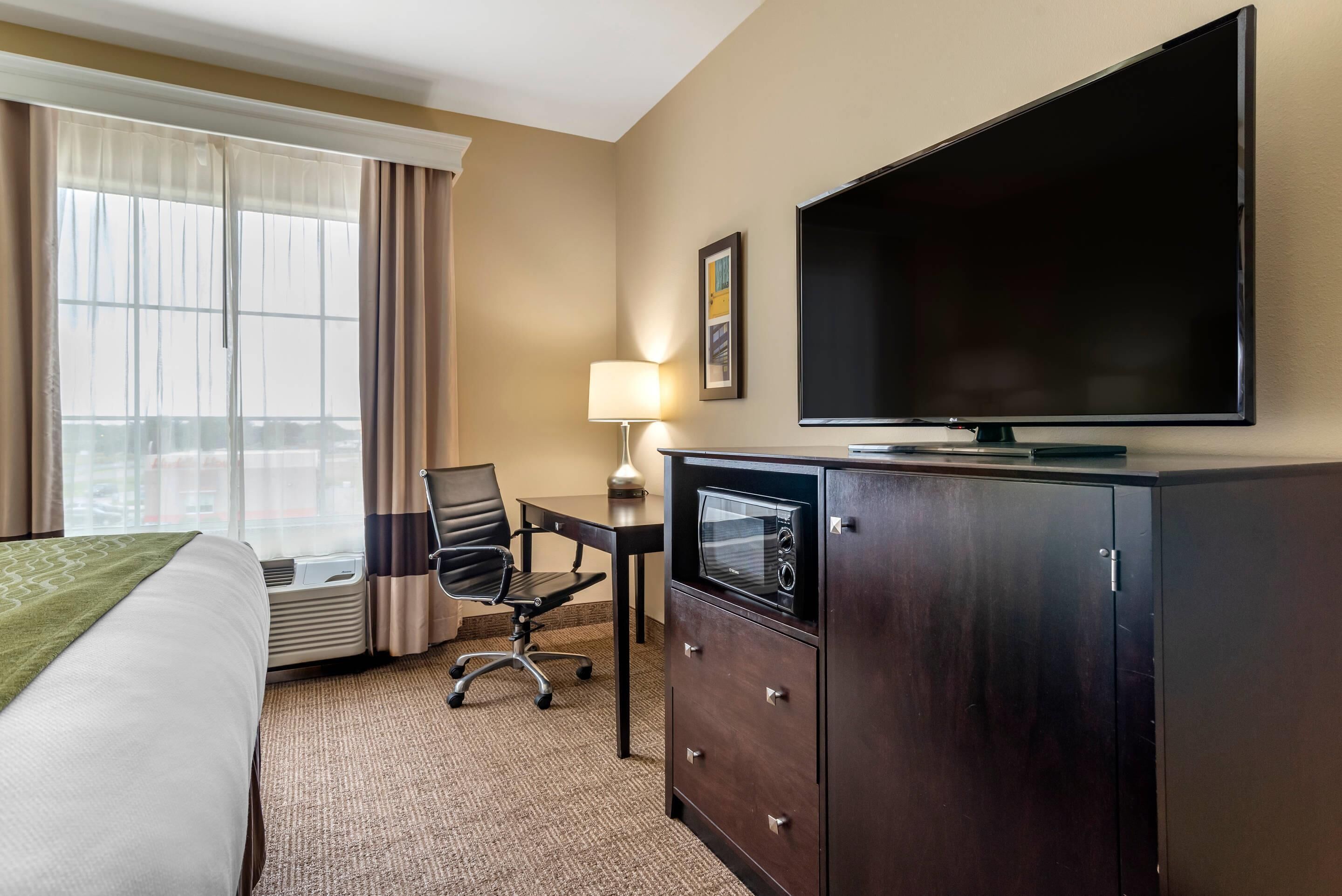 A hotel room with a bed, a desk with a chair, a television, and a minibar.