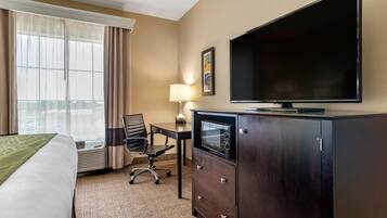 A hotel room with a bed, a desk with a chair, a television, and a minibar.