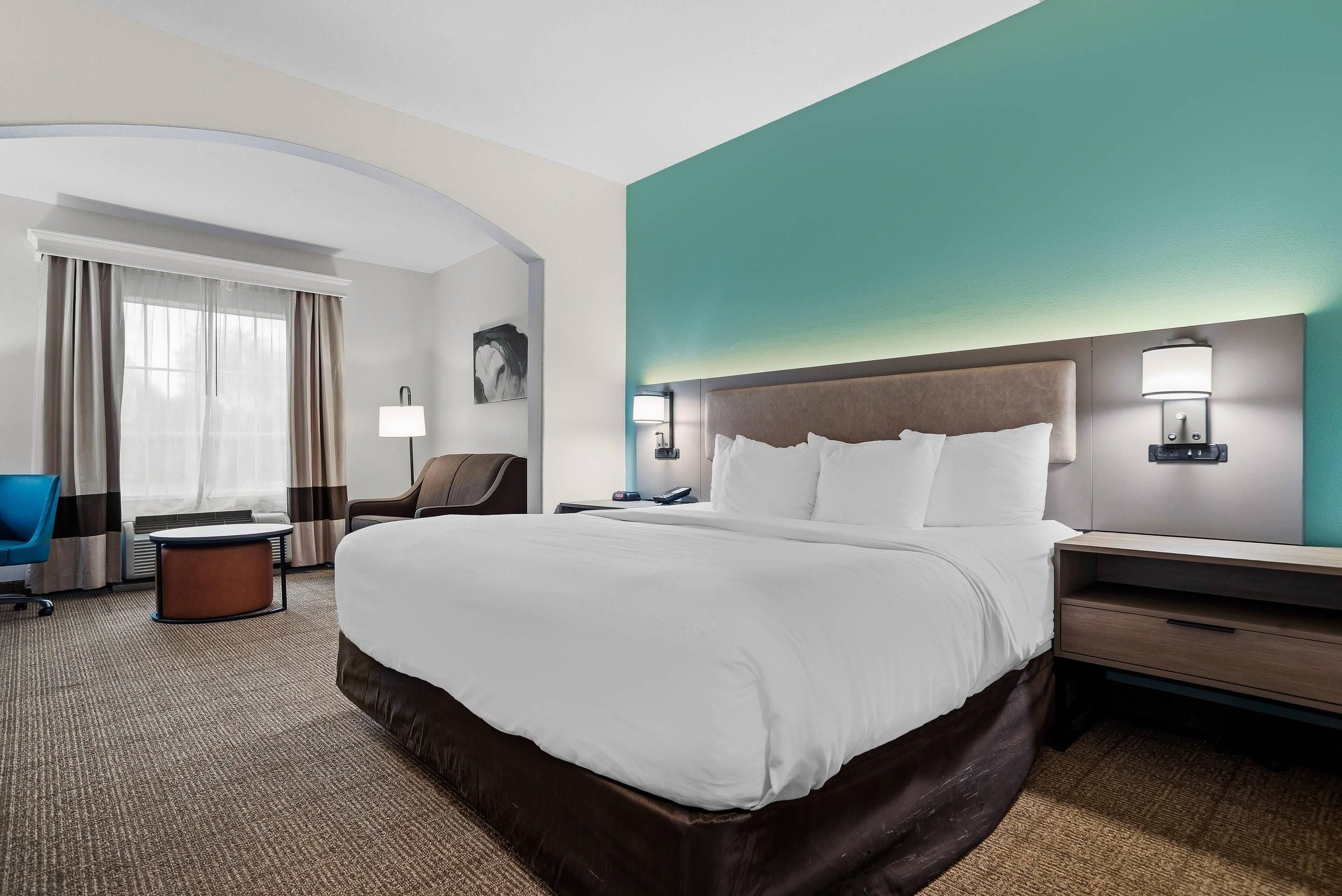 A hotel room with a large bed, a desk, a chair, and a desk lamp.