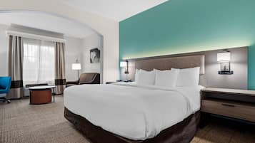 A hotel room with a large bed, a desk, a chair, and a desk lamp.