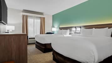 A hotel room with two beds, a desk, a television, and a window with curtains.