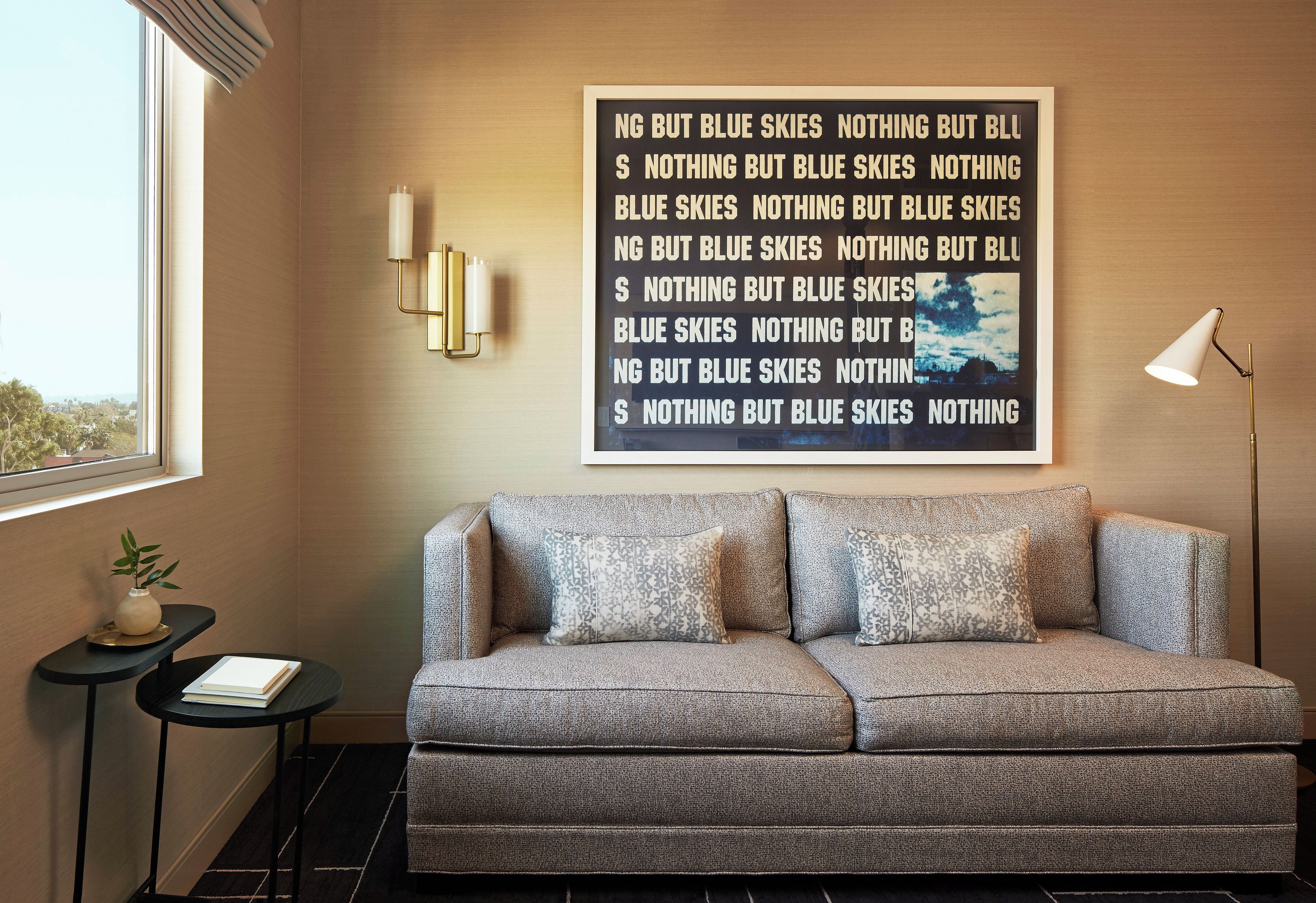 A room with a grey sofa, a wall-mounted light fixture, and a framed text on the wall.